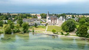Seehotel Schloss Klink @Privathotels Dr. Lohbeck, im Vordergrund der See und im Hintergrund das Schlosshotel, eingerahmt von Baeumen.